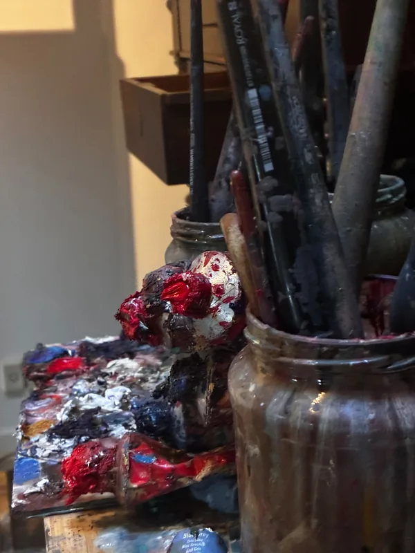 Penselen in een glazen pot, ernaast een klodder rode, blauwe en witte verf.